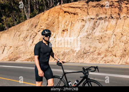 Junger männlicher Radfahrer in schwarzer Sportbekleidung, der mit seinem Fahrrad auf einer Straße unterwegs ist Stockfoto