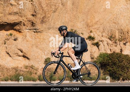 Seitenansicht eines Radfahrers in schwarzer Sportbekleidung auf seinem Fahrrad Stockfoto