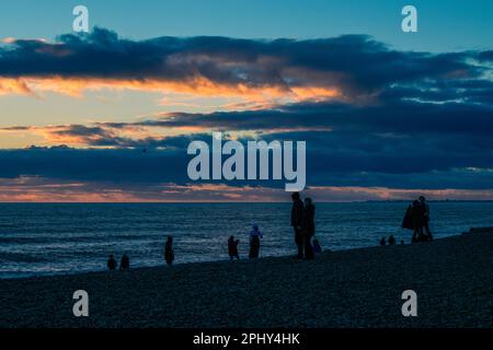 Die Leute beobachten den Sonnenuntergang am Strand in der Dämmerung Stockfoto