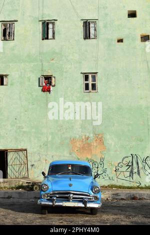 Ein blauer Oldtimer parkt vor dem grünen Gebäude. Die Fenster dieses Hauses in verschiedenen Dimensionen und die Graffiti spiegeln den Charme des wider Stockfoto
