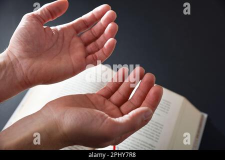 Religiöser Mann betet mit getrennten Händen nach oben und religiöses Buch im Hintergrund auf schwarzem Tisch. Draufsicht. Stockfoto