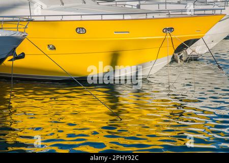 Der Rumpf einer gelben Luxusyacht, deren leuchtende Farbe sich im Wasser des Jachthafens von Puerto Banus, Marbella, Spanien, widerspiegelt Stockfoto