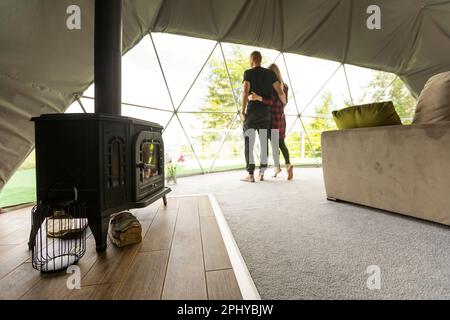 Ein Paar, das die Natur aus Geo-Dome-Zelten betrachtet. Grün, blau, orangefarbener Hintergrund. Gemütlich, Camping, Glamping, Urlaub, Urlaub Lifestyle Konzept. Malerisch Stockfoto