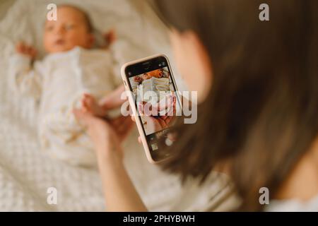 Mutter fotografiert Baby-Junge mit Handy. Stockfoto