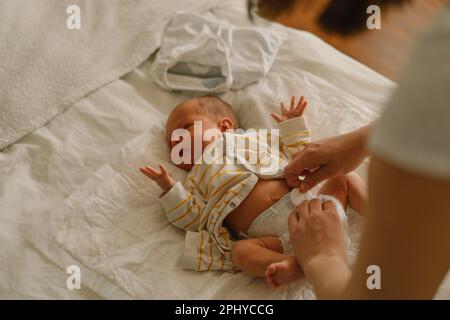 Glückliche junge Mutter, die mit dem Baby spielt, während sie seine Windel im Bett wechselt. Stockfoto