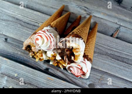 Eiscreme Vanille und Schokoladenzapfen mit Schokolade- und Karamellsoße und Nüssen in knusprigen Waffeln, Schmelzen von kaltem Eis in einem Stockfoto