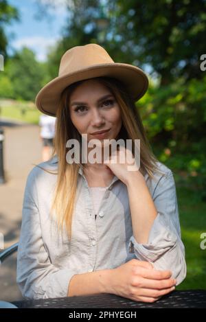 Eine junge, wunderschöne blonde Frau mit breitem Hut und blassgrauem Hemd, die in die Kamera schaut. Stockfoto