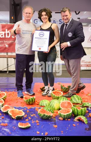 Hamburg, Deutschland. 30. März 2023. Muhamed Kahrimanovic (l) und Lucrezia Albanese legen das Zertifikat am Platteninstitut für Deutschland vor, das sie zum Weltrekord für die Zerschlagung von 16 Wassermelonen in einer Minute auf dem Magen des Sportlers erklärt. Rechts Olaf Kuchenbecker vom Platteninstitut für Deutschland. Kredit: Ulrich Perrey/dpa/Alamy Live News Stockfoto