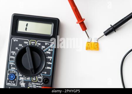 Prüfung auf defekte farbige Kfz-Sicherung mit Digitalmultimeter auf weißem Hintergrund, flach verlegt, Draufsicht Stockfoto