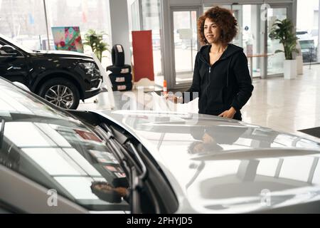 Eine lächelnde multirassische Frau steht in der Nähe eines neuen Autos Stockfoto