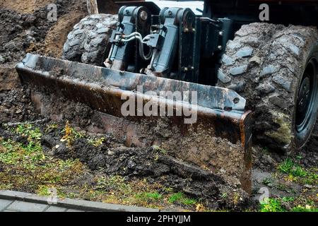 Radtraktor mit Schaufel räumt an bewölkten Regentagen den Boden frei. Schmutzige Bulldozer-Schaufel Nahaufnahme... Stockfoto