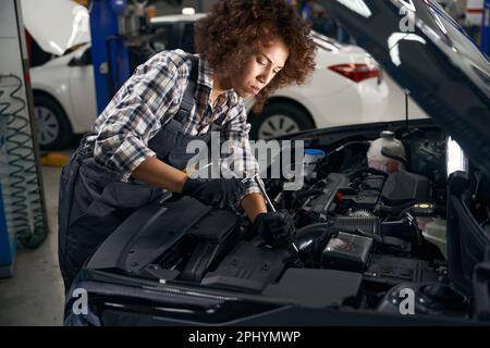 Multirassenmitarbeiter in der Autowerkstatt in Schutzhandschuhen repariert den Motor Stockfoto