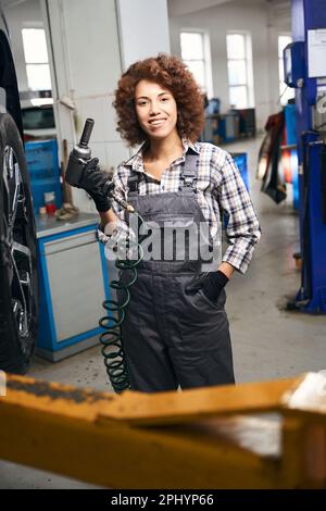 Glückliche junge Frau, die einen pneumatischen Schraubenzieher in der Hand hält Stockfoto