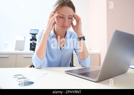 Die Frau hat Kopfschmerzen während der Arbeit am Laptop im Zimmer Stockfoto