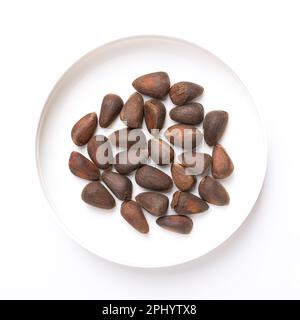 Samen einer Steinkiefer, in einem weißen Kunststoffdeckel, von oben. Nüsse aus einem Kegel von Pinus cembra, auch bekannt als Schweizer, Arolla oder österreichische Steinkiefer. Stockfoto