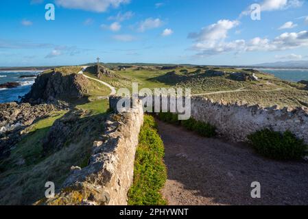 Pfad vom Leuchtturm Twr Mawr mit Blick auf eines der Kreuze und Ruinen der Kirche St. Dwynwens auf Ynys Llanddwyn, Anglesey, Nordwales. Stockfoto