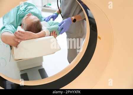 Erwachsener Mann, der in der Kammer eines MRT-Geräts liegt und seine Hände hochhält Stockfoto