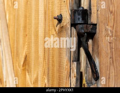 Alte, schwarze Scharnierarmaturen, hergestellt von einem Schmied. Armaturen an einer alten Holztür eines alten Schuppens Stockfoto