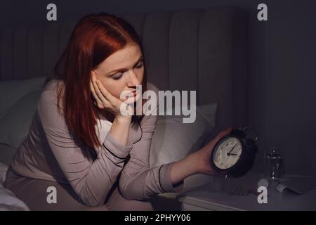 Eine Frau, die an Schlaflosigkeit leidet und auf den Wecker im Schlafzimmer schaut Stockfoto