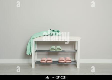 Elegante Aufbewahrungsbank mit verschiedenen Paar Gummipantoffeln an der weißen Wand im Flur Stockfoto