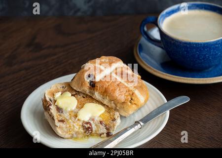 Ein Osterbrötchen mit heißem Kreuz, getoastet und serviert mit Butter, die auf dem warmen Brötchen schmilzt. Traditionell am Karfreitag in Großbritannien serviert Stockfoto