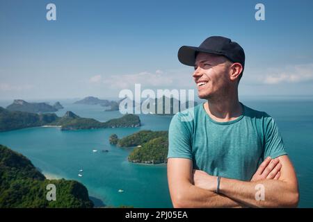 Porträt eines lachenden Mannes auf einem Hügel gegen eine Gruppe tropischer Inseln im Meer, Thailand Stockfoto