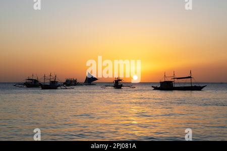 Traditionelle Boote auf der Tablas Strait, hinter dem Sonnenuntergang von Angol Beach, Boracay Island, Visayas Archipel, Philippinen Stockfoto