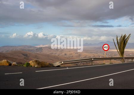 Blick von den Bergen auf das zentrale Tiefland. Wolkiger Himmel. Schöne neue Straße mit Geschwindigkeitsbegrenzung. Mirador de Morro Velosa, Betncuria, Fuerteventura, Spanien Stockfoto