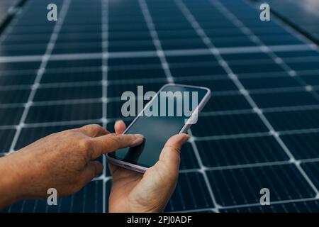 Nahaufnahme eines jungen Ingenieurs, der an sonnigen Tagen das Smartphone mit der Hand auf dem Hintergrund hält, Konzept für umweltfreundliche alternative Energie. Hochwertiges Foto Stockfoto