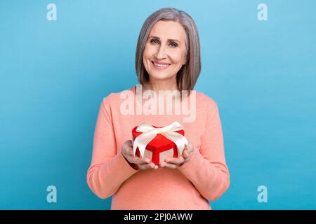 Foto des bezaubernden, charmanten weiblich gekleideten Korallenhemds mit rotem Herzform Geschenkbox isolierter blauer Hintergrund Stockfoto