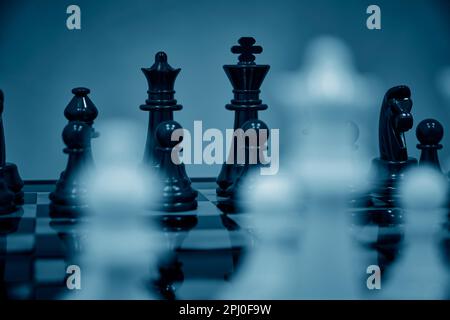 Schwarze Schachfiguren Hintergrund Weiße verschwommene Schachfiguren stehendes Schachbrett Stockfoto