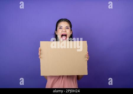 Junge Frau hält ein Schild mit ihren Händen mit einem überraschenden Ausdruck auf einem isolierten lila Hintergrund Stockfoto