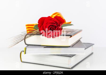 Nahaufnahme von roter Rose und Weizenohr auf einem Stapel Bücher für Diada de Sant Jordi. Tradition des St.-Jordi-Tages in Katalonien. Katalanisches Buch und Rosenblüten-Tag Stockfoto