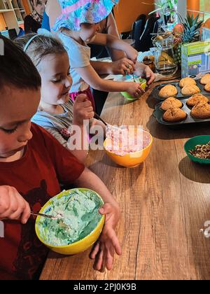 Gruppe von Kindern, die Cupcakes backen, Zutaten zubereiten, Toppings, Streuseln zum Dekorieren von Keksen. Kinder lernen kochen, arbeiten zusammen Stockfoto