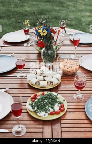 Abendessen in einem Apfelgarten auf Holztisch mit Salaten und Wein mit Blumen dekoriert. Nahaufnahme des Tisches mit Essen für Familienessen vorbereitet Stockfoto