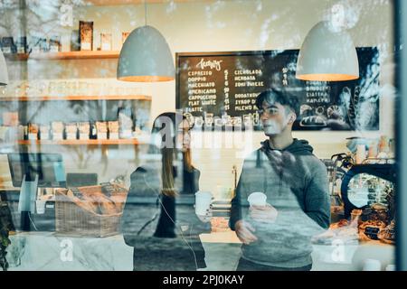Freunde unterhalten sich, halten Kaffeetassen in der Hand, stehen in einem Café und warten auf ihre Bestellungen. Mann und Frau machen eine Pause und trinken Kaffee Stockfoto