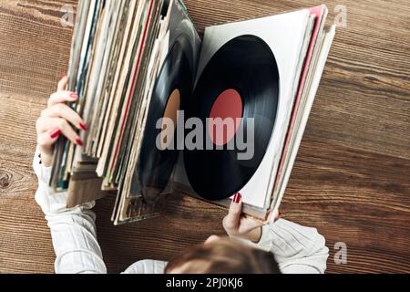 Vinyl-Schallplatten spielen. Musik von einem Vinyl-Plattenspieler hören. Retro- und Vintage-Musikstil. Frau mit analogem LP-Plattenalbum. Stapel alt Stockfoto