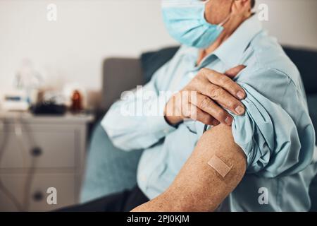 Älterer Patient, der die Hemdhülse mit einem Gips anstelle einer Injektion des Impfstoffs hält. Covid-19- oder Coronavirus-Impfung. Mann mit Gesichtsmaske Stockfoto