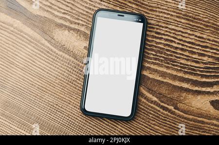 Smartphone-Modell mit weißem, leeren, isolierten Bildschirm auf Holzhintergrund. Schwarzes Mobiltelefon, Draufsicht, flache Unterlage mit Platz für Kopien. Bereit Stockfoto