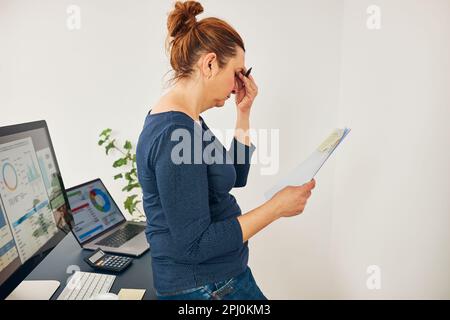 Unternehmerin, die müde und gestresst ist. Verwirrte und verwirrte Geschäftsfrau, die an ihrem Schreibtisch im Büro steht und sich Gedanken um die Aufbewahrung von Dokumenten macht. Fru Stockfoto