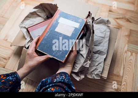 Eine Frau, die Bücher aus dem Karton nimmt. Paket wird ausgepackt. Weibliche Hände mit Büchern Stockfoto