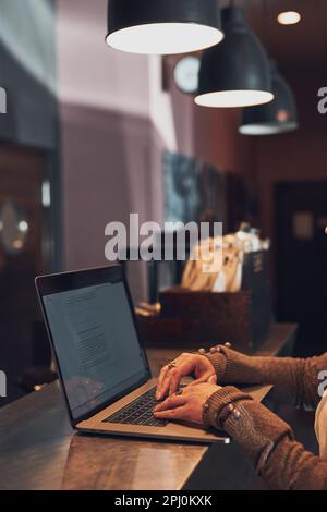 Frau, die aus der Ferne an ihrem Laptop arbeitet und ihre Arbeit verwaltet, sitzt am Tisch in einem Café. Weibliche Hände tippen auf Laptop-Tastatur Stockfoto