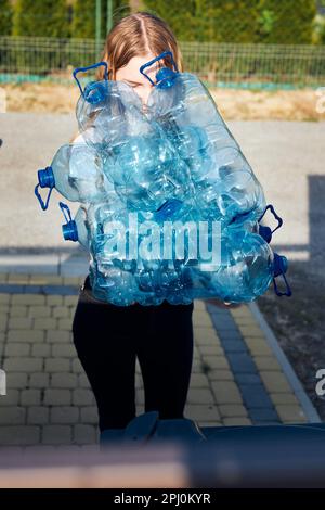 Junge Frau wirft leere gebrauchte Plastikwasserflaschen in den Abfalleimer. Sammeln von Kunststoffabfällen zum Recycling. Konzept der Plastikverschmutzung und auch Stockfoto