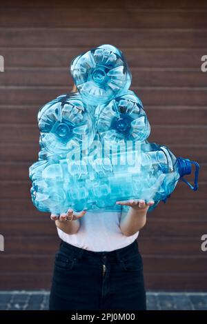 Junge Frau wirft leere gebrauchte Plastikwasserflaschen in den Abfalleimer. Sammeln von Kunststoffabfällen zum Recycling. Konzept der Plastikverschmutzung und auch Stockfoto