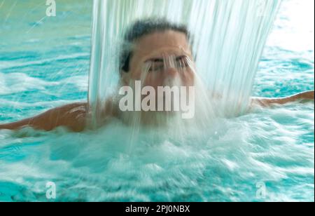 Frauengesicht Entspannen Sie sich in einem Hydromassage-Pool mit fallendem Wasser bei Langzeit-Exposition in der Schweiz. Stockfoto