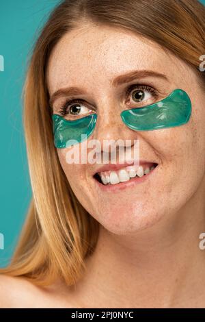 Porträt einer glücklichen Frau mit Sommersprossen und Kollagenflecken unter den Augen, die auf einem türkisfarbenen Stockbild lächeln Stockfoto