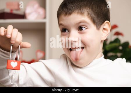 Valentinstag und Kinder. Der lustige 5- oder 6-jährige Junge hat ein Herz und zeigt seine Zunge Stockfoto