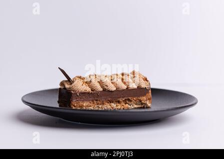 Eine schwarze Keramikplatte mit einem reichen Schokoladenkuchen, gekrönt mit einer Schicht cremigen, weißen Zuckerglases Stockfoto