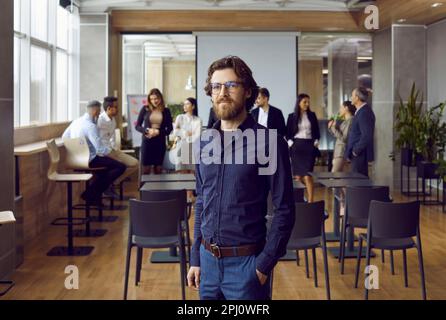 Porträt eines ernsthaften, selbstbewussten Geschäftsmanns, der vor dem Hintergrund seines Büroteams im Amt steht. Stockfoto
