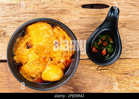 Blick von oben auf köstliches hausgemachtes würziges Hühnercurry mit Kartoffeln, Kokosmilch und Chili in schwarzer Keramikschüssel mit Fischsauce mit rotem und grünem Stück Stockfoto